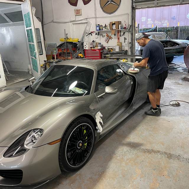 Technician polishing a silver Porsche 918 Spyder inside Gold Coast Collision Center in Pompano Beach