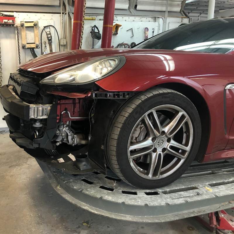 Red Porsche Panamera with the front end torn down for collision repair at Gold Coast Collision Center in Pompano Beach