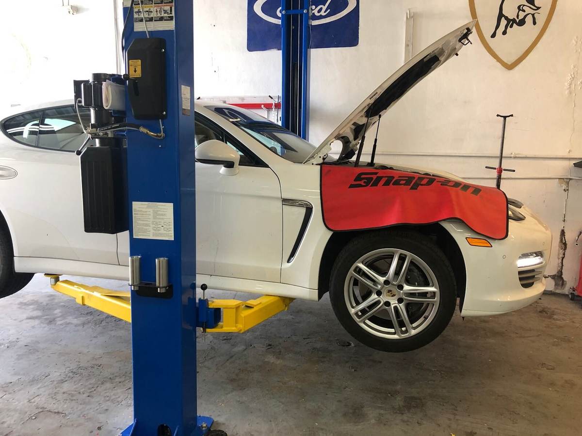 White Porsche Panamera on a two-post lift with the hood up for mechanical repair at PorscheWorks in Pompano Beach